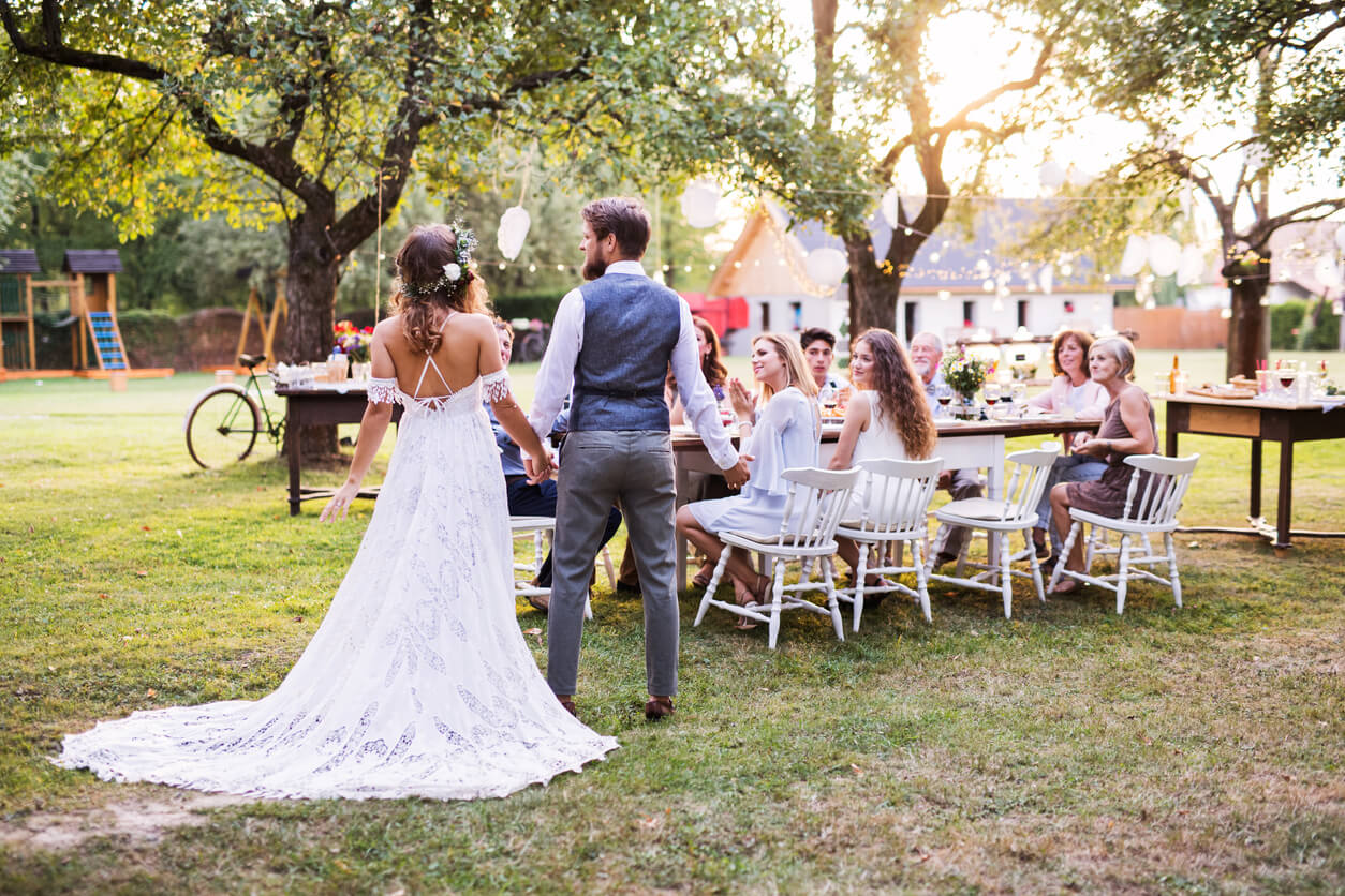 A newly-married couple at their backyard wedding speaks to a table of guests
