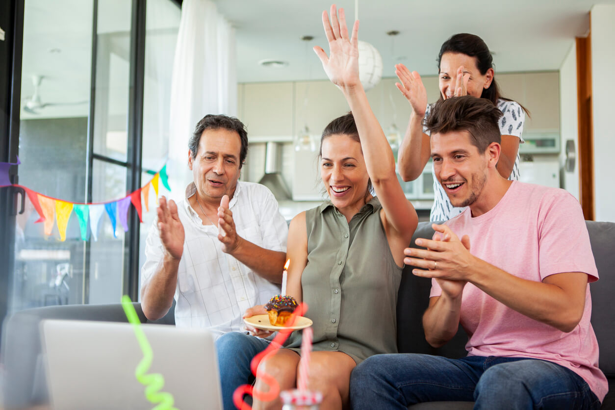 A family of four celebrates and holds a cupcake while sitting in front of a laptop and attending a hybrid event