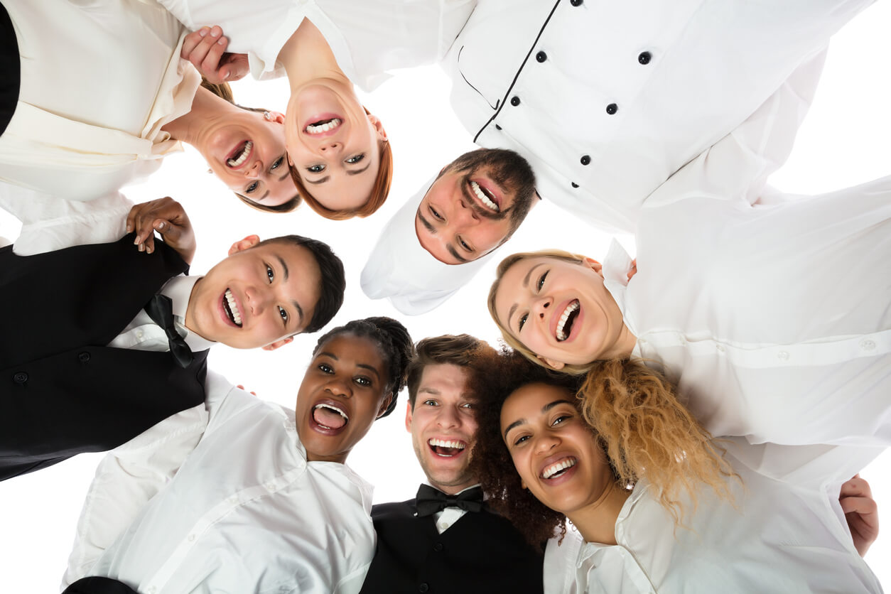 A happy full-service catering staff standing in a circle looking down and smiling
