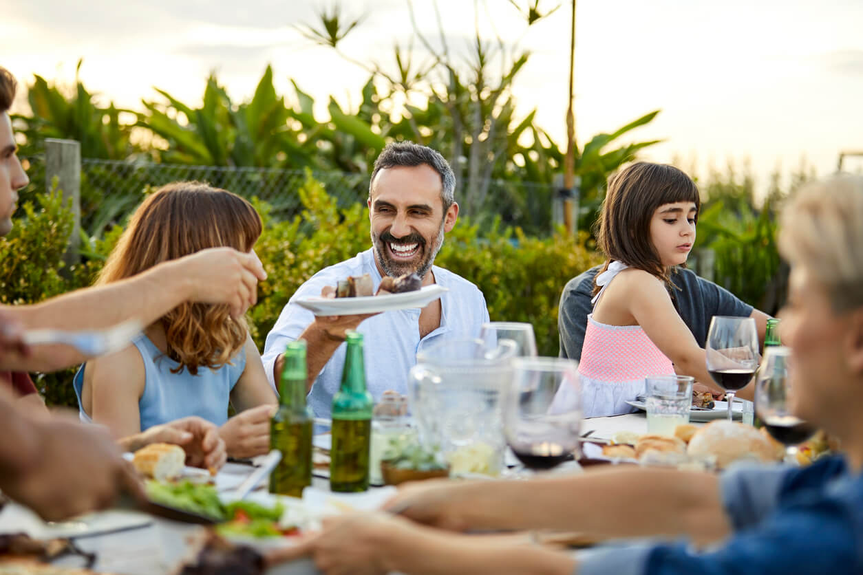 A group of adults and children sitting at a table laughing and mingling outdoors during a summer BBQ