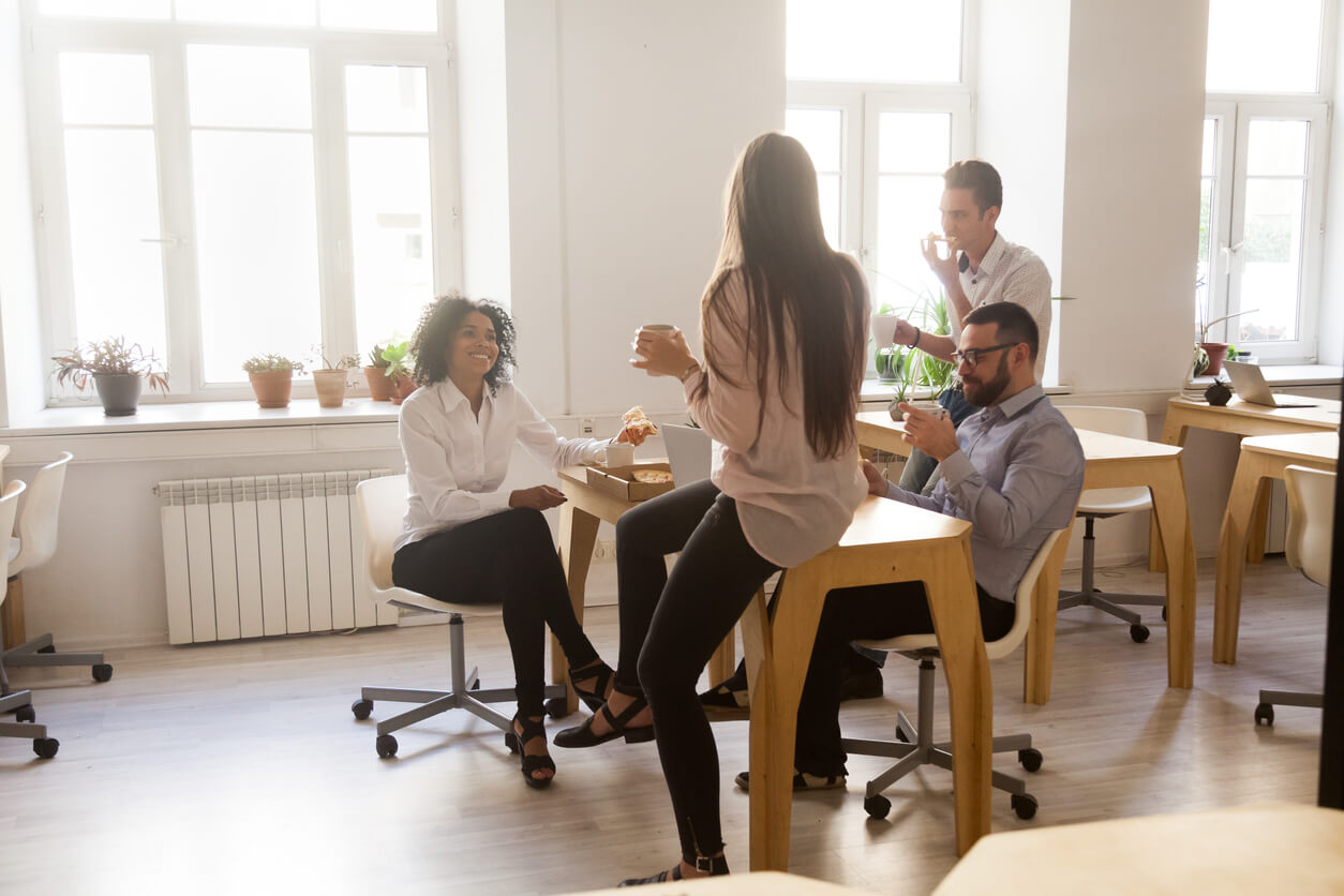 Four coworkers happily sitting around a table enjoying office snacks and talking