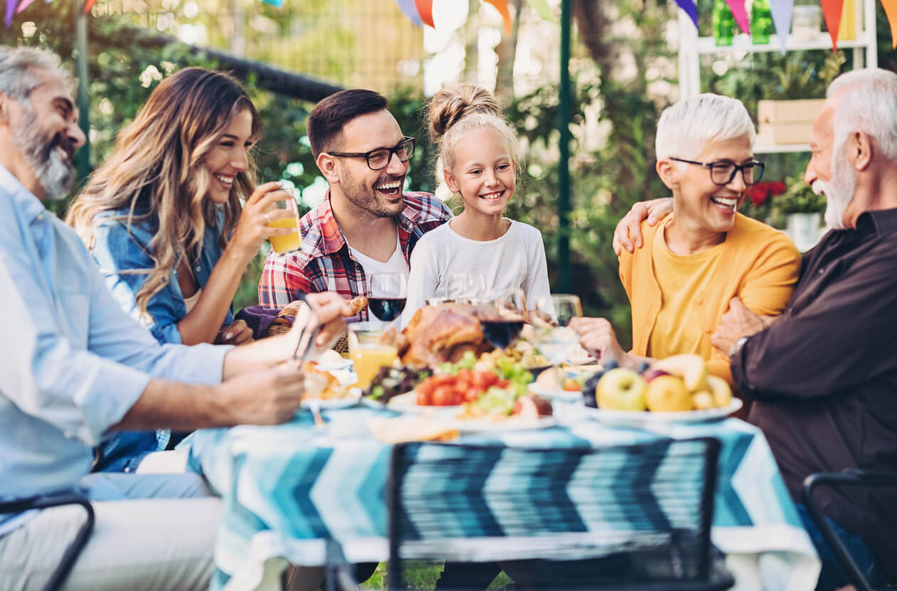 A happy family sits around an outdoor table and enjoys the food at a catered family event